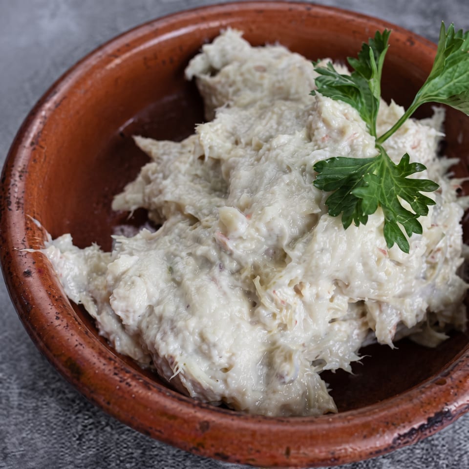 Creamy shredded salad garnished with parsley, served in a rustic terracotta bowl on a dark tabletop.