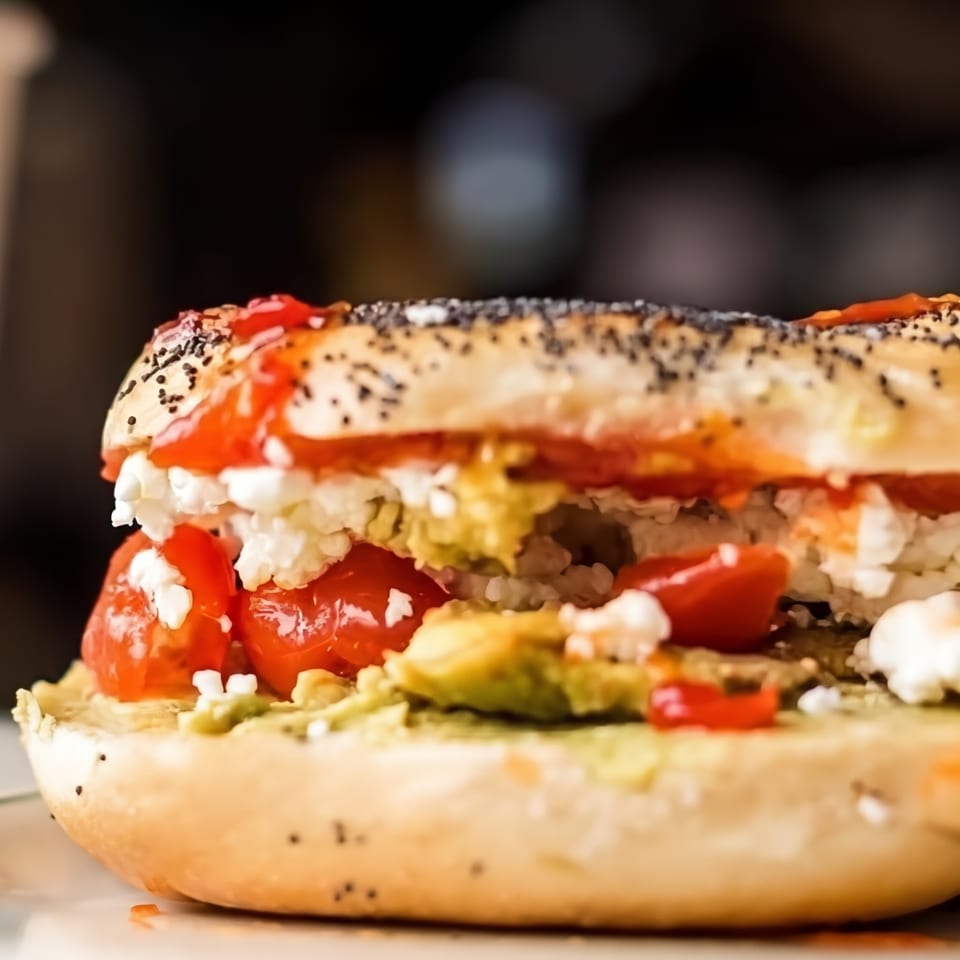 Close-up of a loaded bagel sandwich with sesame seeds, cream cheese, vegetables, and deli meat.